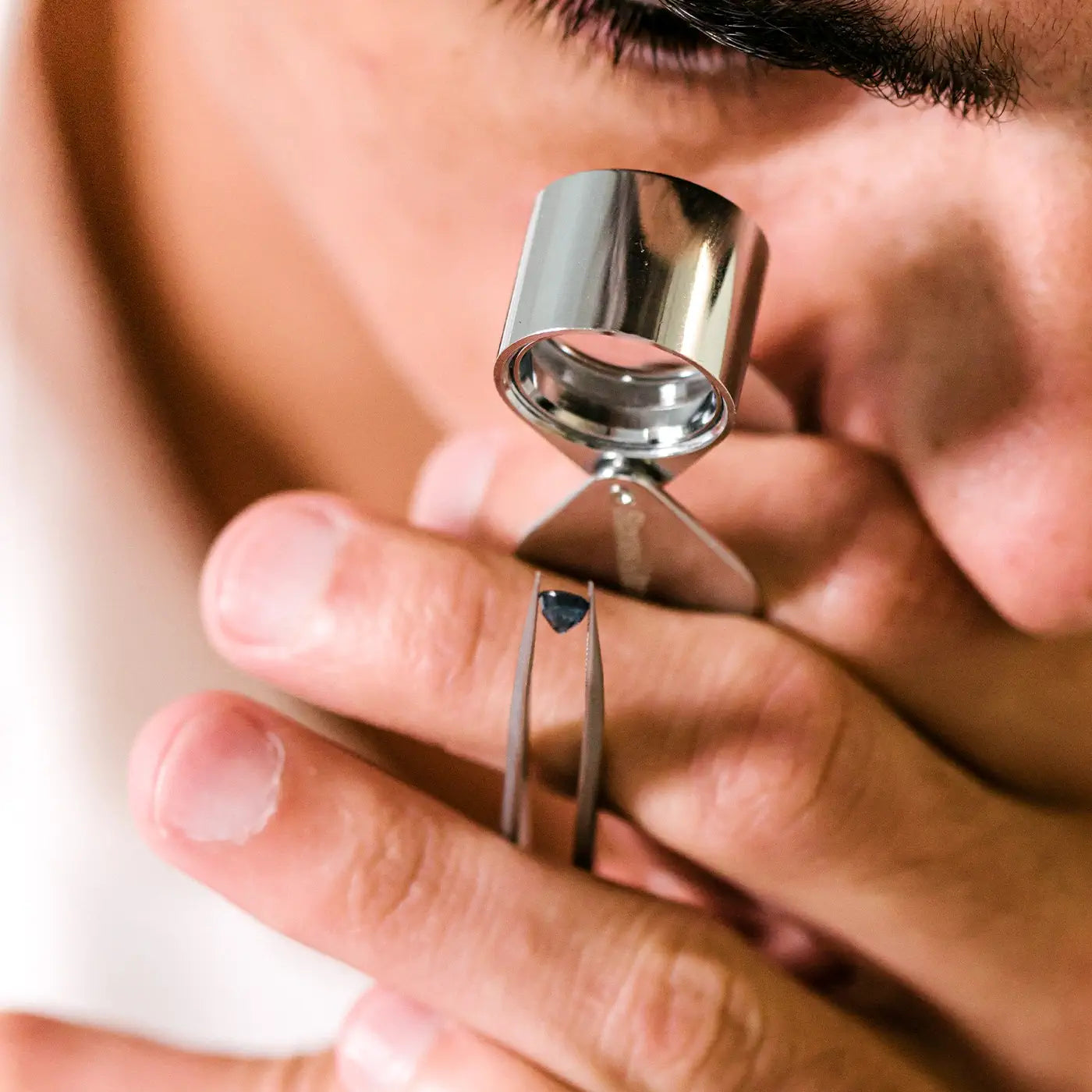 Gemmologist inspecting a natural blue sapphire with a loupe to check its clarity.