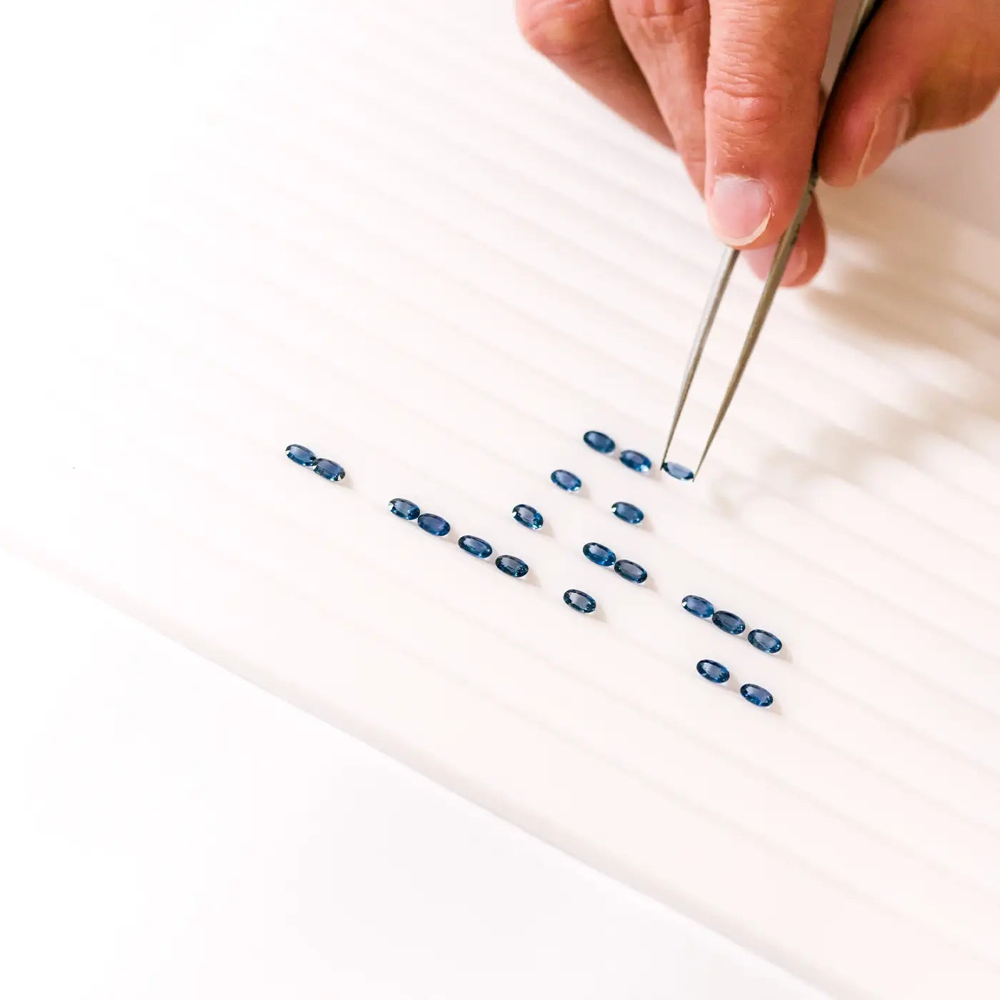 Gemmologist carefully sorting natural sapphires on a tray to craft a custom bracelet.