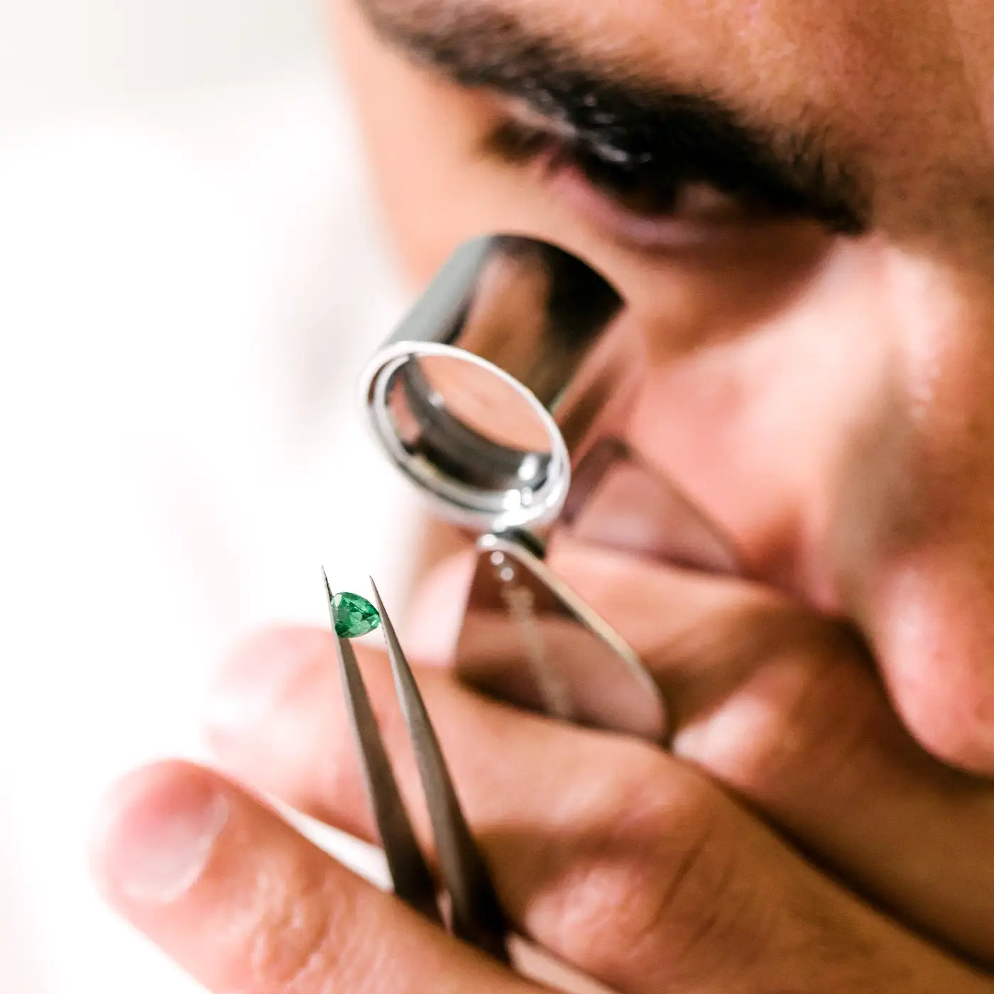 Gemmologist inspecting a natural emerald with a loupe to check its clarity.